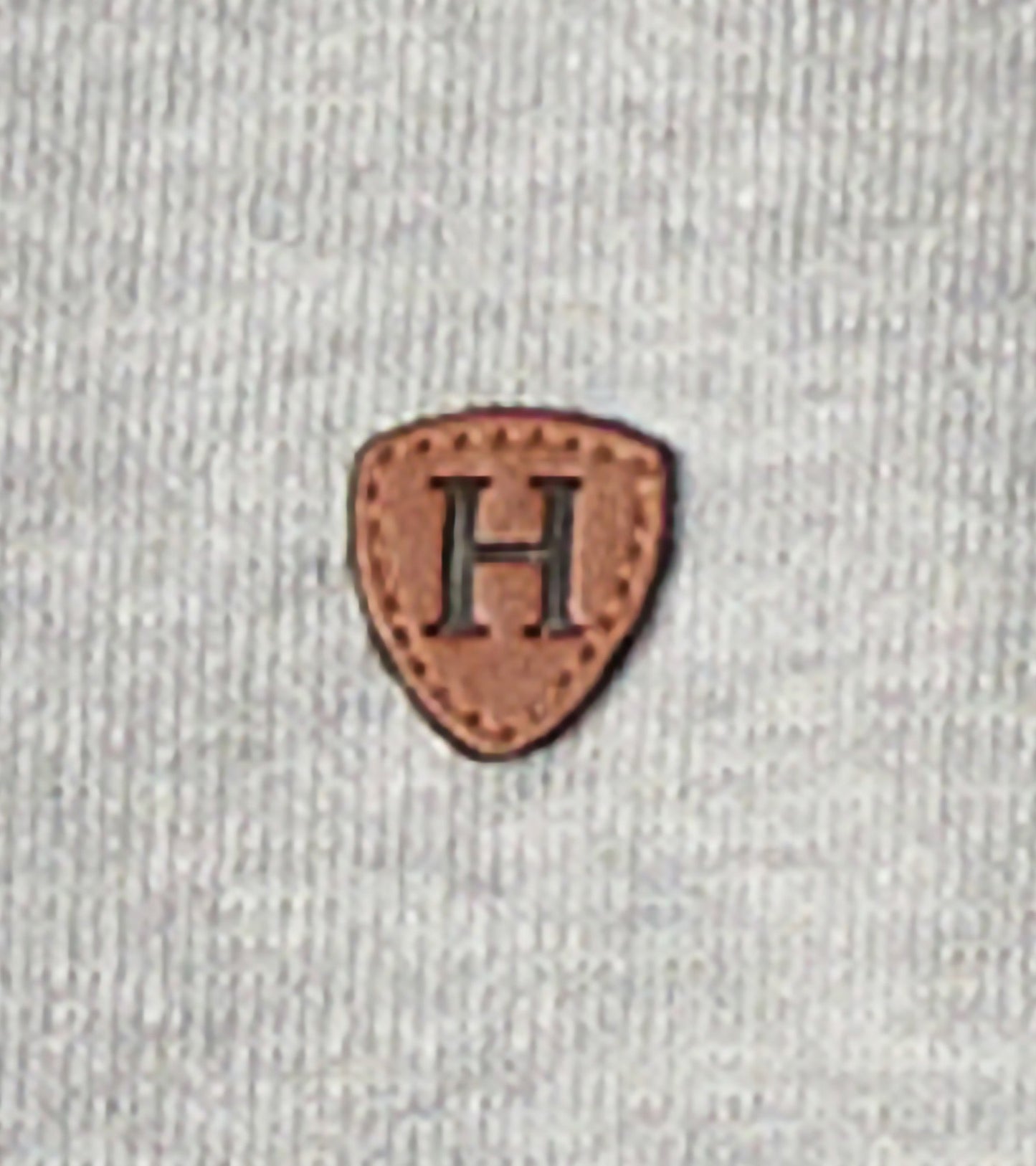 Grey zip-up hoodie featuring a textured fabric and a brown leather patch with an embossed letter "H.