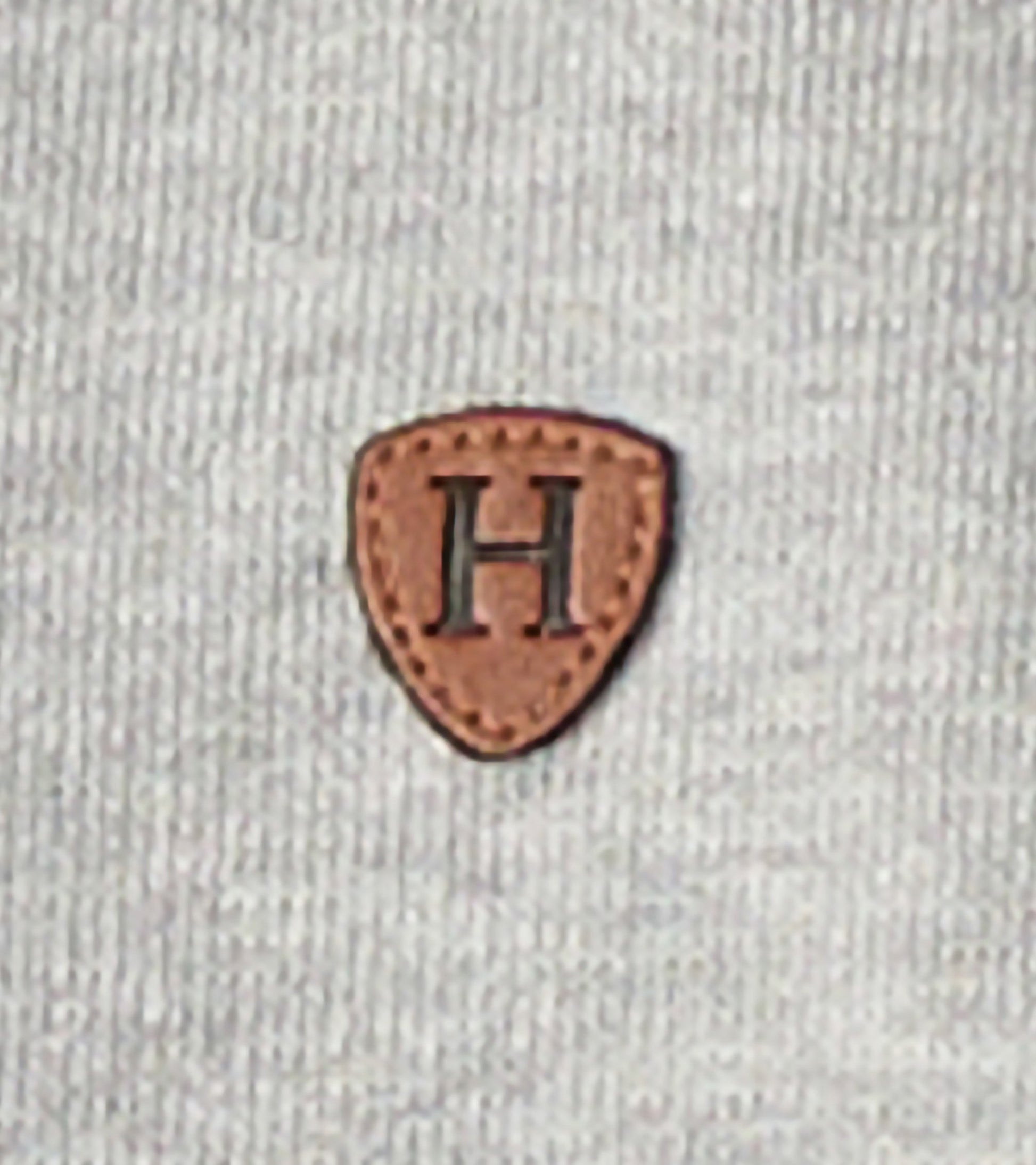 Grey zip-up hoodie featuring a textured fabric and a brown leather patch with an embossed letter "H.