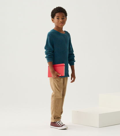 Boy wearing a Moroccan blue knit sweater with tan pants, holding a red notebook
