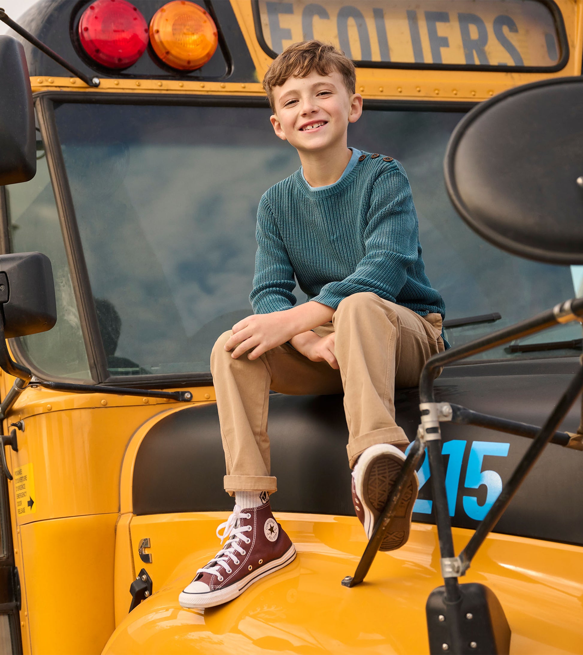 Boy in a Moroccan blue knit sweater and tan pants sitting on a yellow school bus