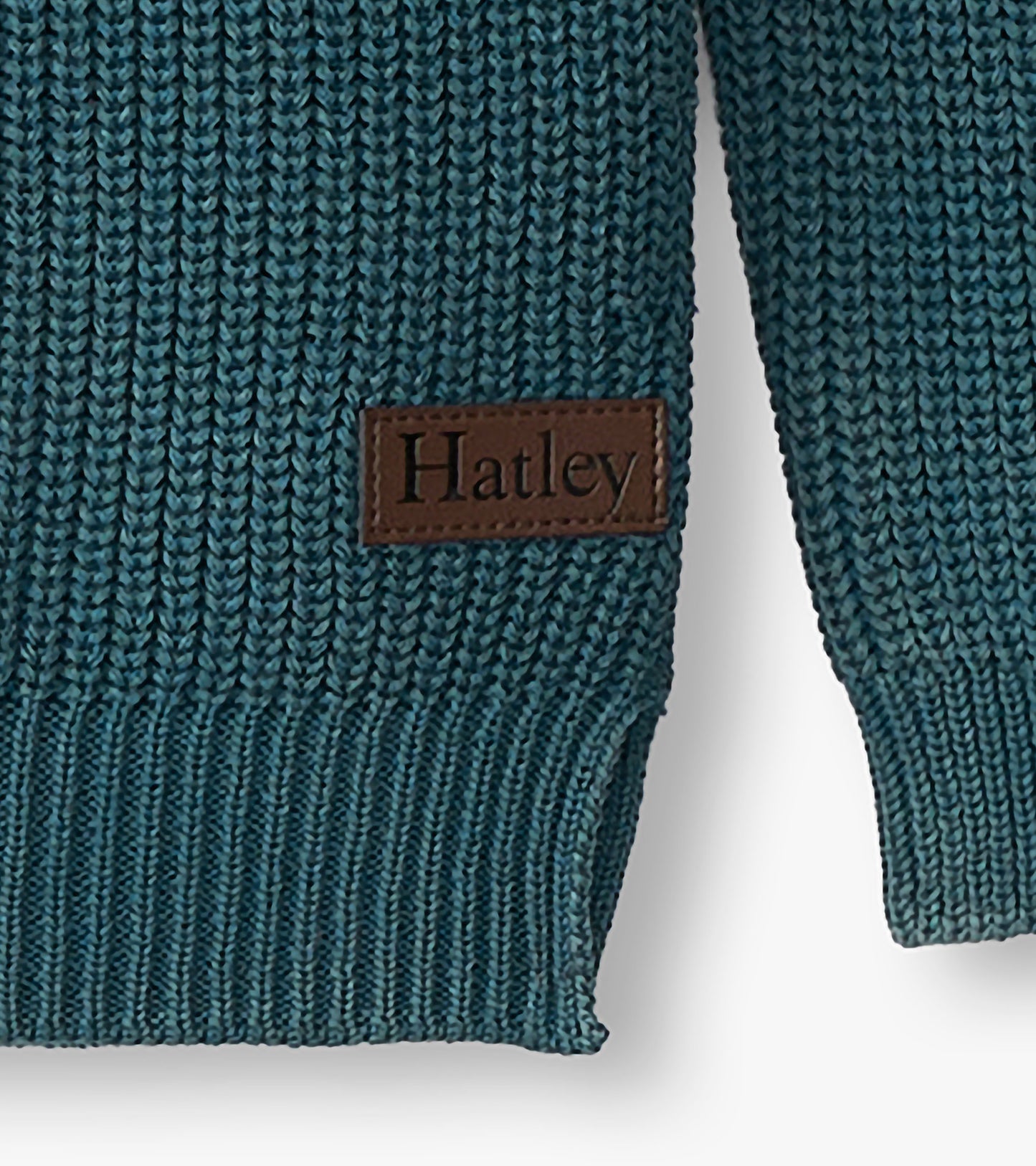 Close-up of the blue sweater hem and sleeve with ribbed knit texture and a brown Hatley logo patch