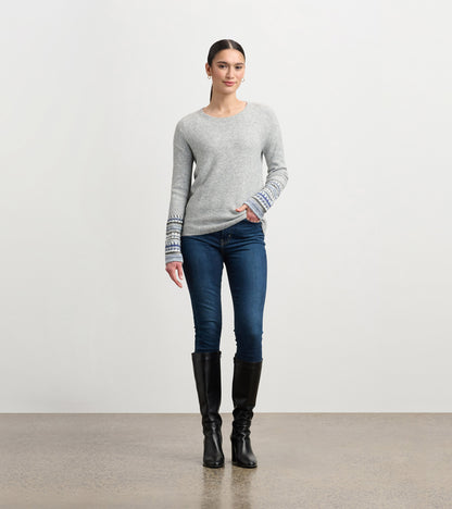 Grey melange sweater with patterned cuffs, featuring a relaxed fit and round neckline, paired with dark jeans and knee-high…