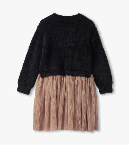 Black fuzzy top with long sleeves paired with a pleated, shimmery rose gold skirt. Back view.