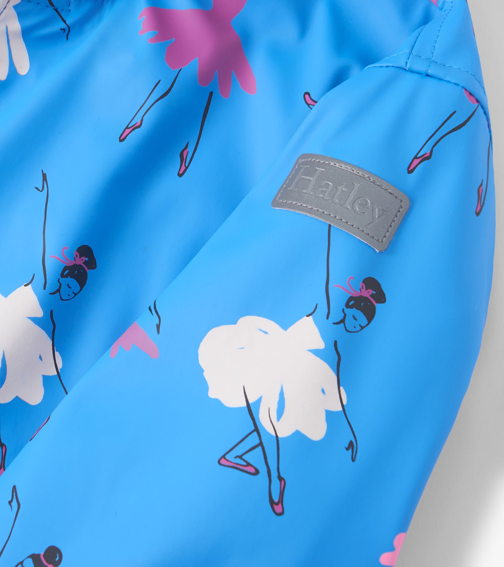 Blue zip-up rain jacket featuring colorful ballet dancer prints and a gray label. Ideal for school or outdoor activities.