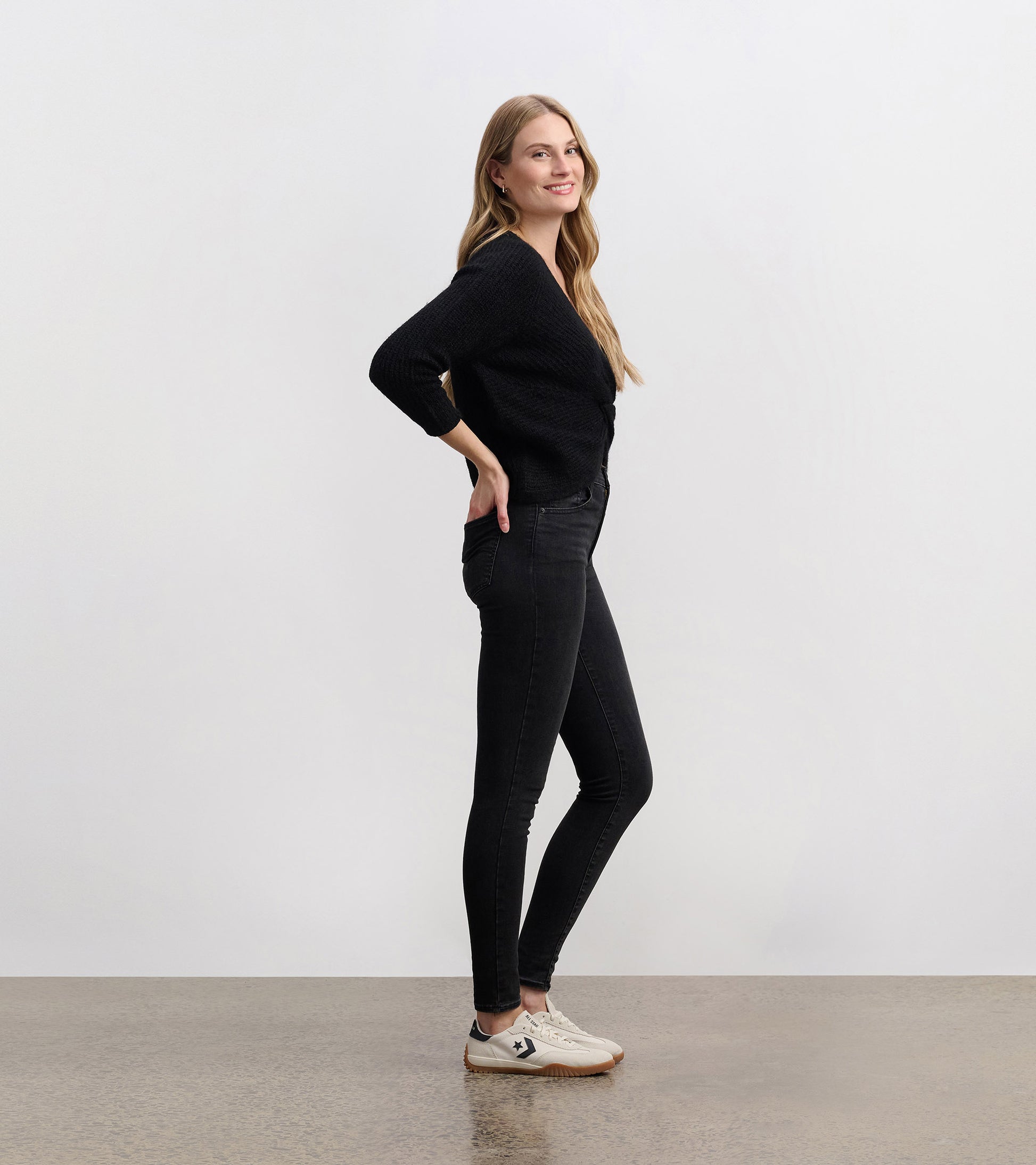 Black crossover sweater with a textured pattern, featuring three-quarter sleeves, styled with black jeans and sneakers.