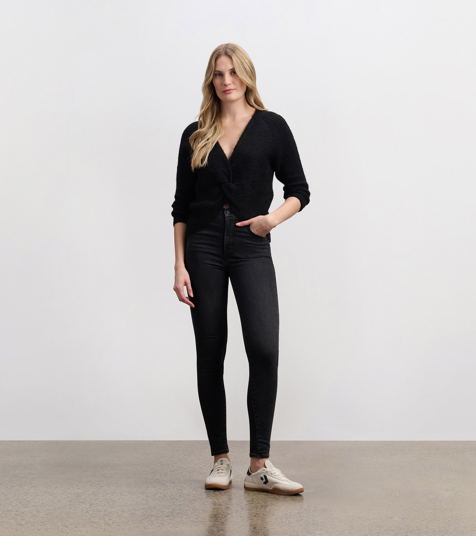 Black crossover sweater with a textured knit, featuring a deep V-neck and three-quarter sleeves, styled with skinny jeans.