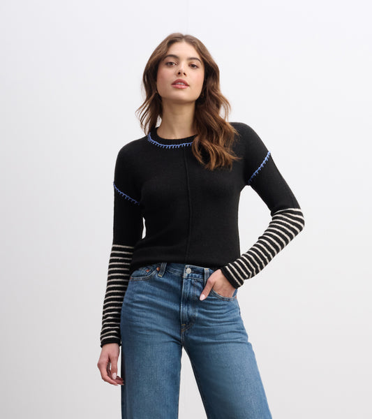 Black sweater with blue stitching and striped sleeves, styled with high-waisted jeans.