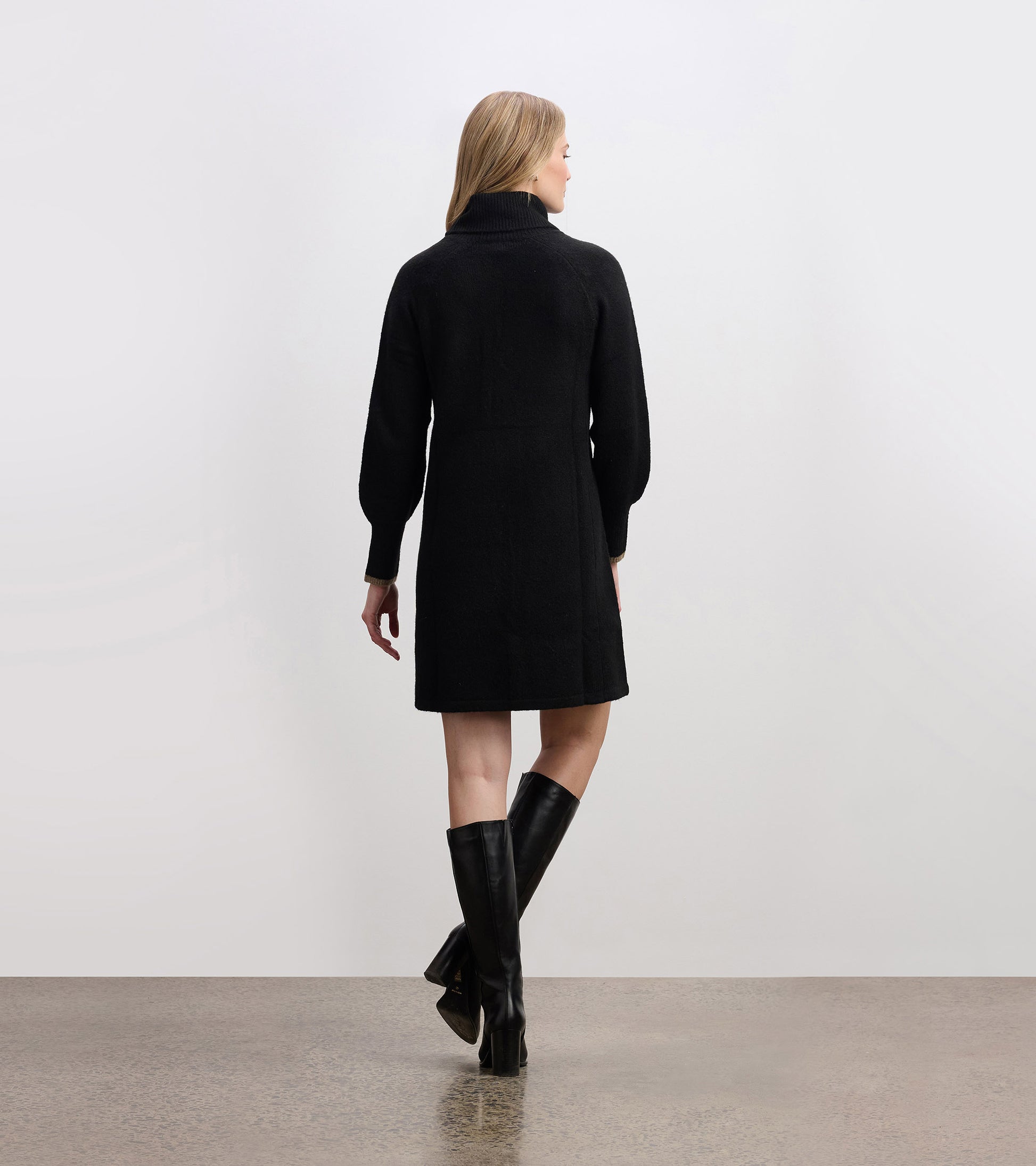 Black swing sweater dress with a high collar and long sleeves, styled with knee-high black boots.