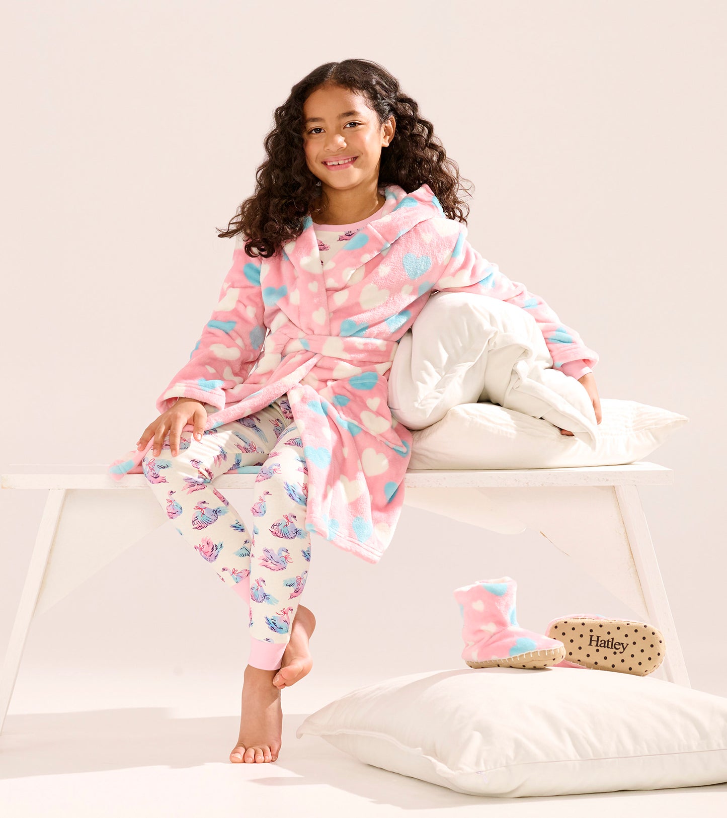 Fuzzy fleece robe in pink with blue hearts, worn by a girl sitting on a bench, paired with patterned leggings and slippers.