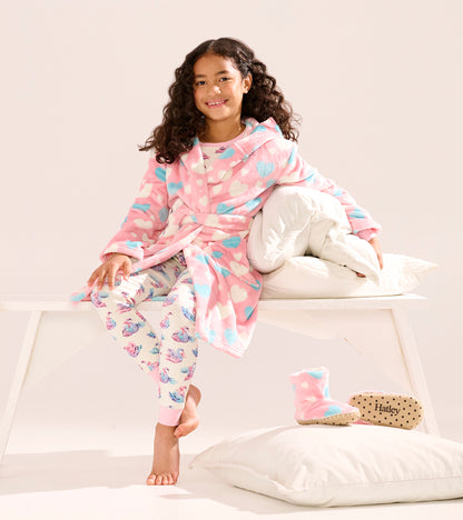 Fuzzy fleece robe in pink with blue hearts, worn by a girl sitting on a bench, paired with patterned leggings and slippers.