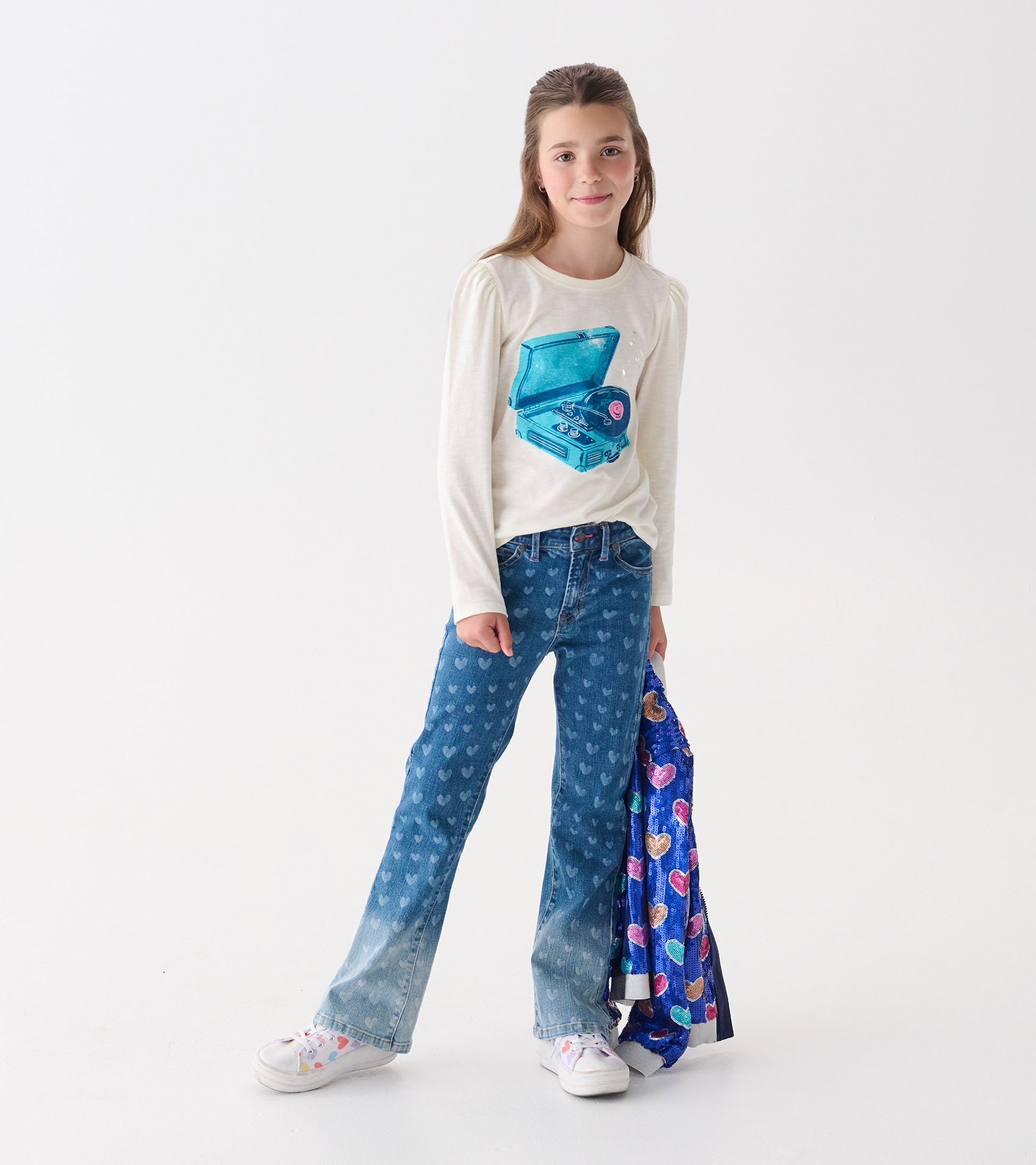 Cream long-sleeve tee featuring a blue graphic of a record player, paired with blue heart-patterned jeans.