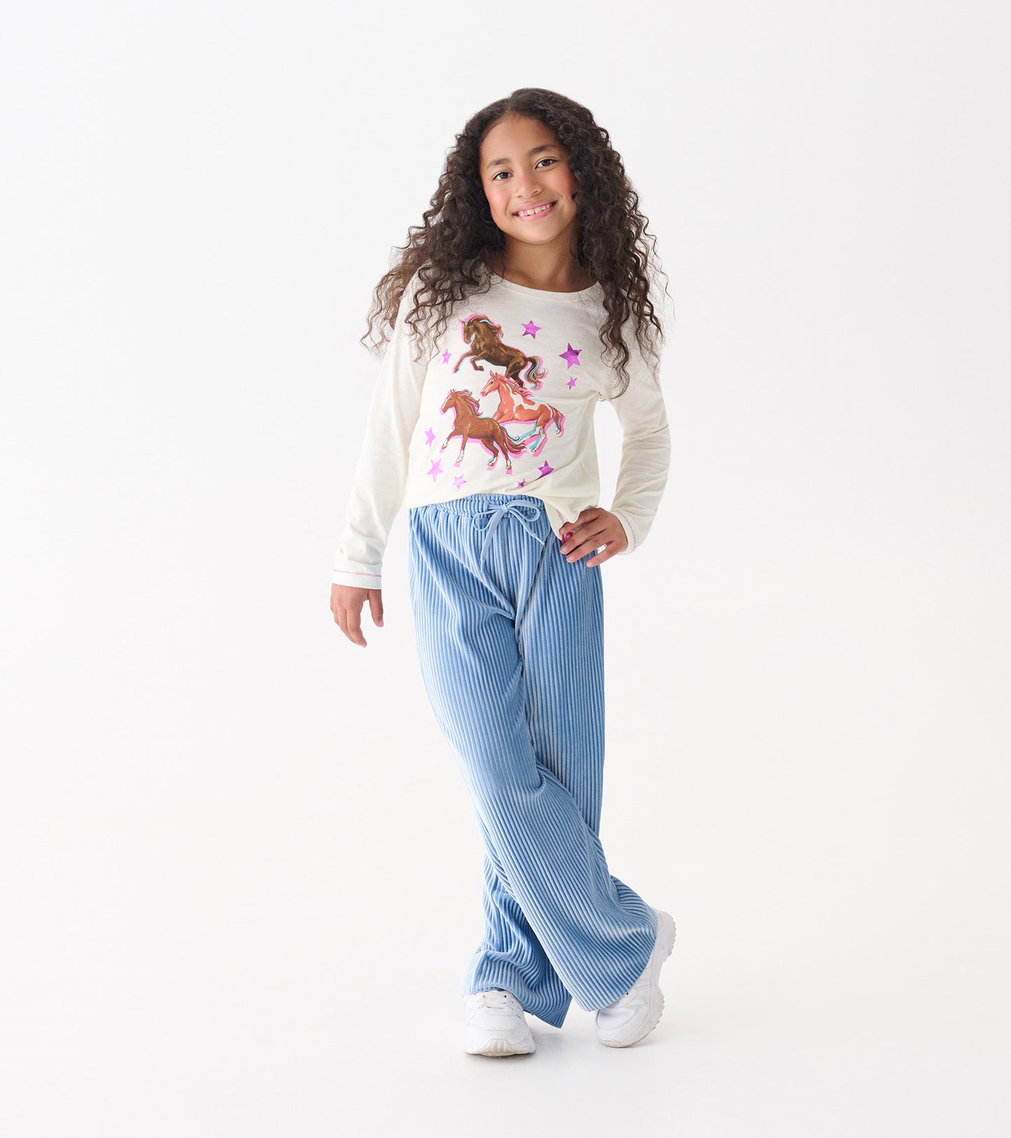 Cornflower blue pleated velour relaxed pants with an elastic waistband, styled with a playful top and sneakers.