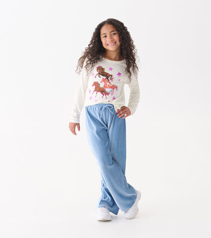 Cornflower blue pleated velour relaxed pants with an elastic waistband, styled with a playful top and sneakers.