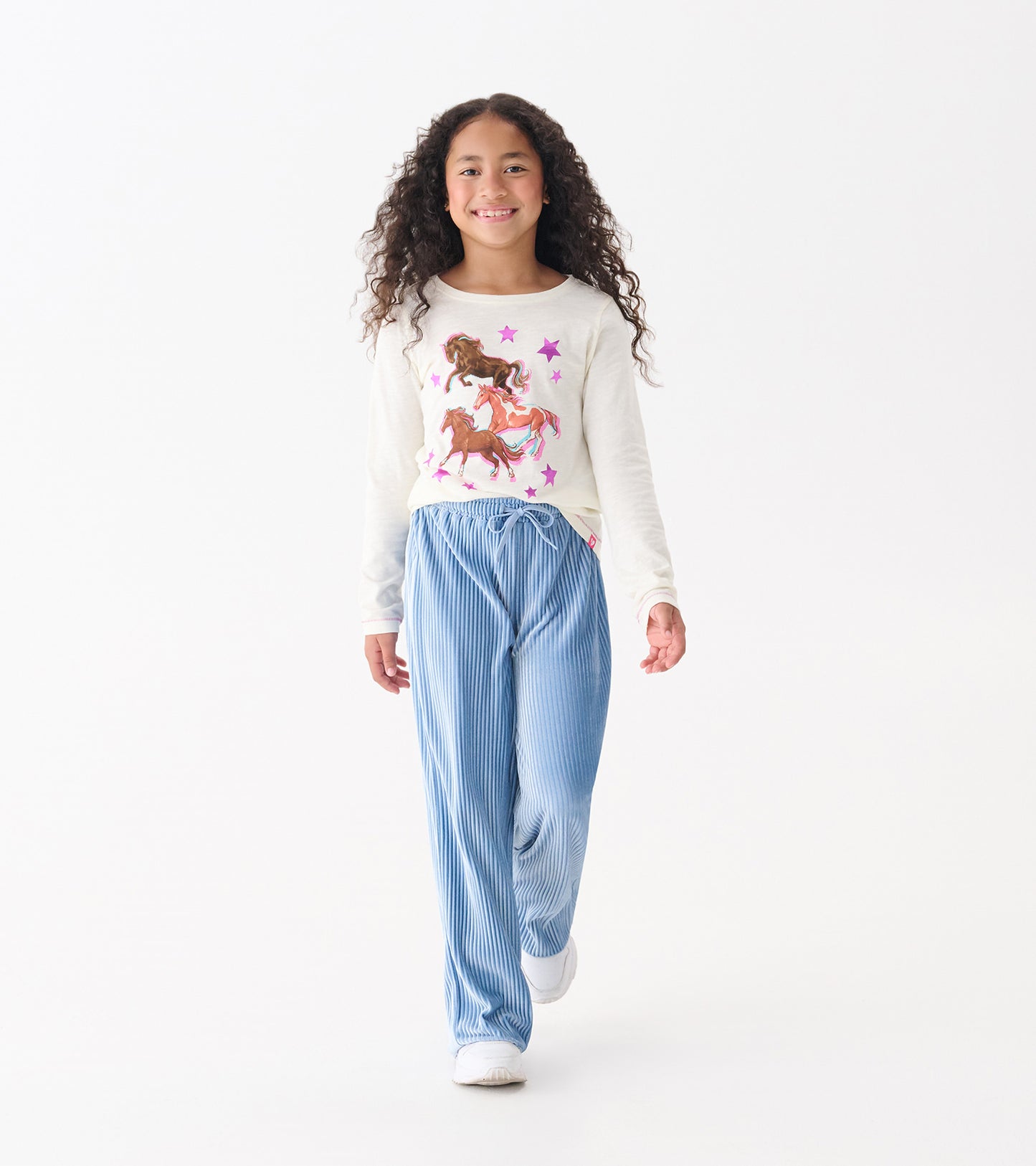 Long sleeve cream graphic tee featuring galloping horses and stars, paired with blue striped pants.