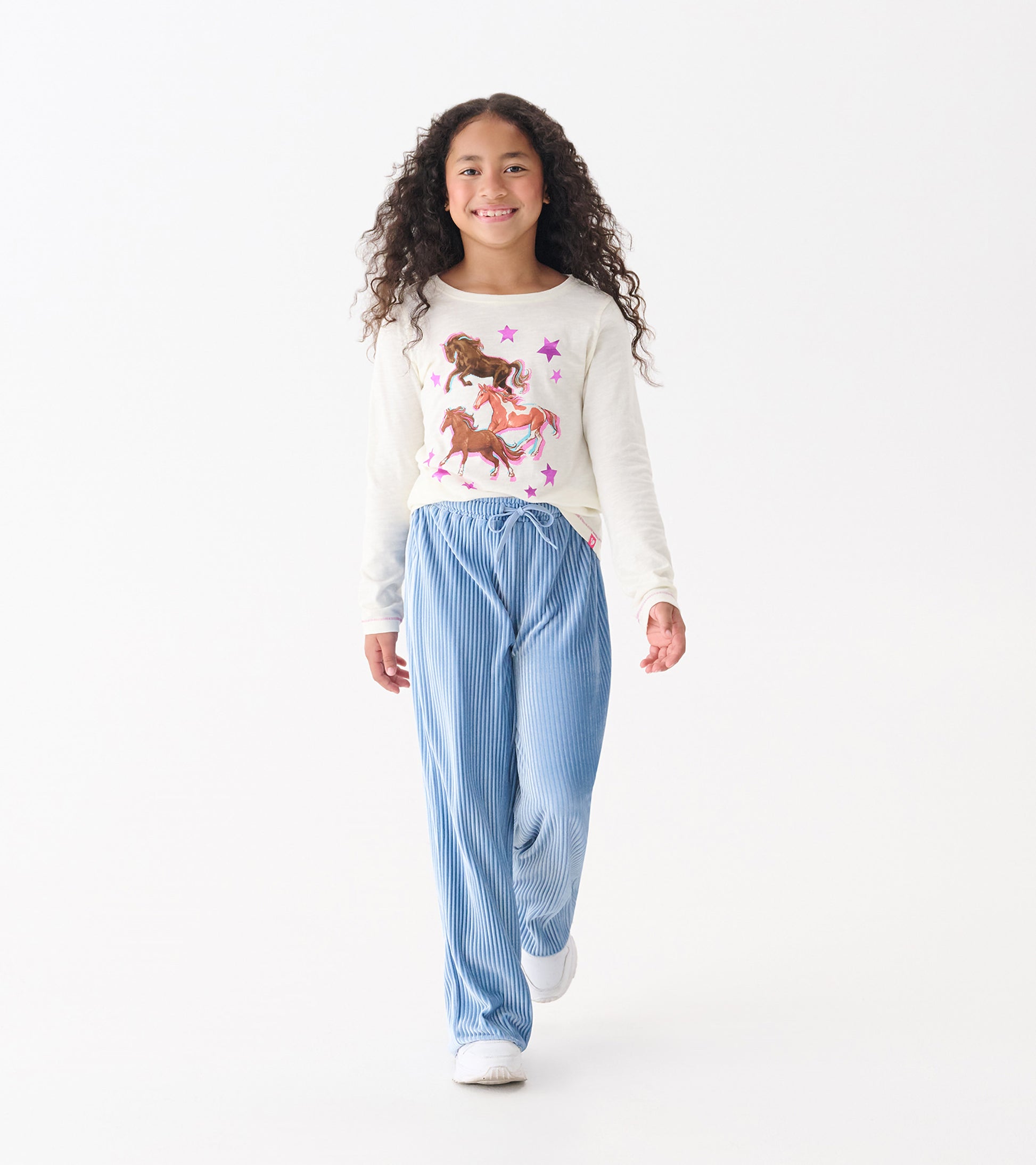 Long sleeve cream graphic tee featuring galloping horses and stars, paired with blue striped pants.