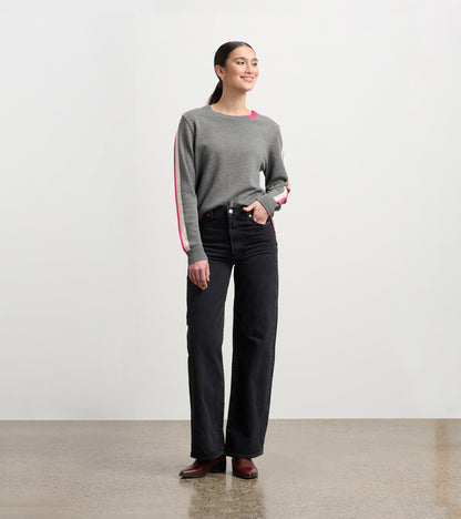 Charcoal sweater with contrasting pink trim, crew neck, and relaxed fit, paired with high-waisted black jeans.
