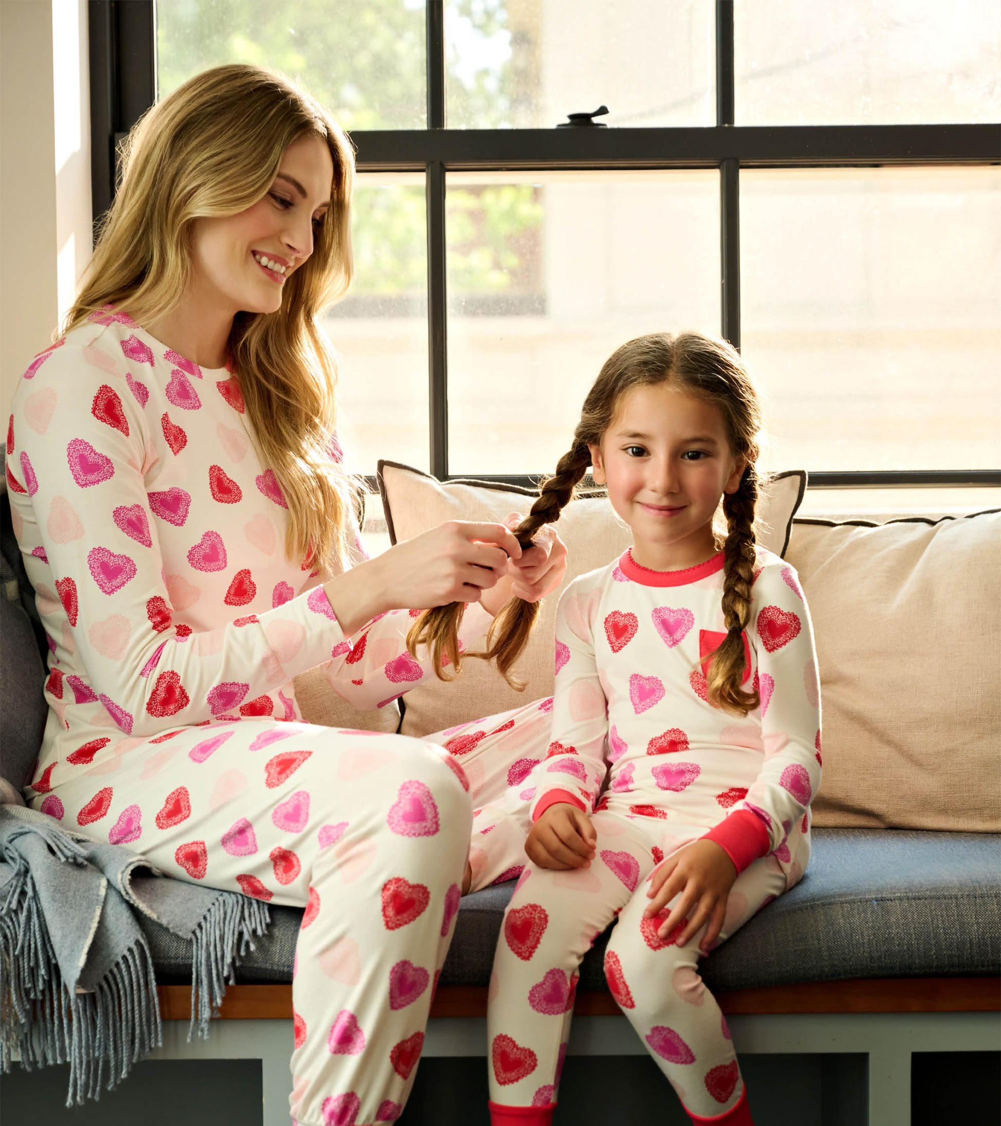 Bamboo pajama set featuring pink and red heart patterns, worn by a woman and girl, sitting on a couch.