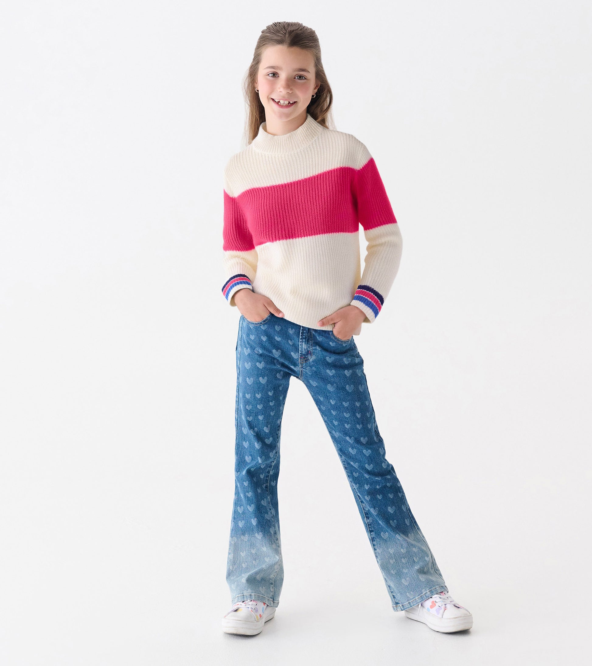 Mockneck sweater in cream with a pink colorblock design and striped cuffs, paired with flared jeans and sneakers.