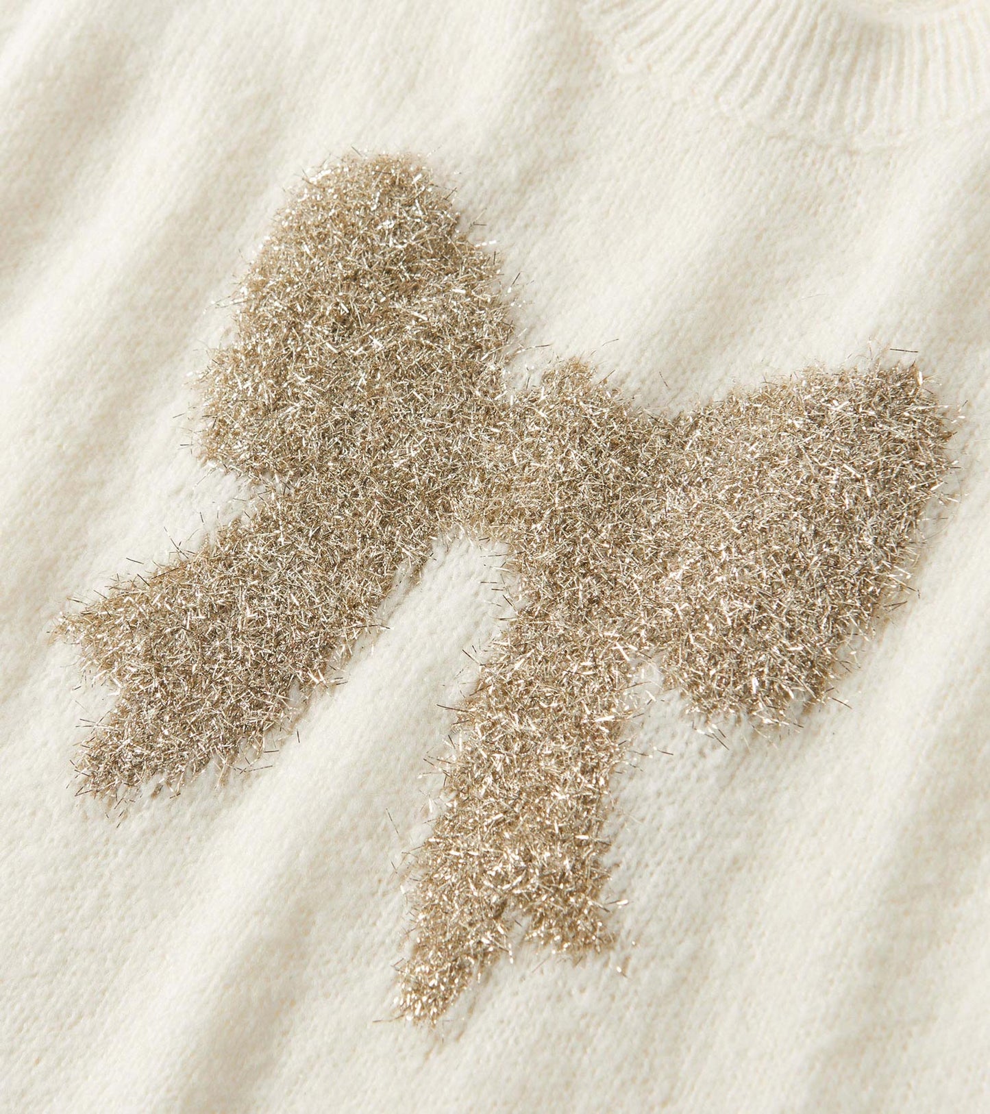 Cream sweater vest featuring a textured gold bow design at the front. Soft knit material with a ribbed neckline.