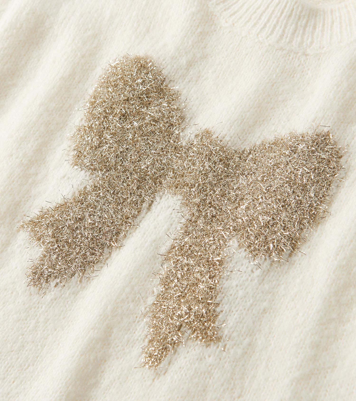 Cream sweater vest featuring a textured gold bow design at the front. Soft knit material with a ribbed neckline.