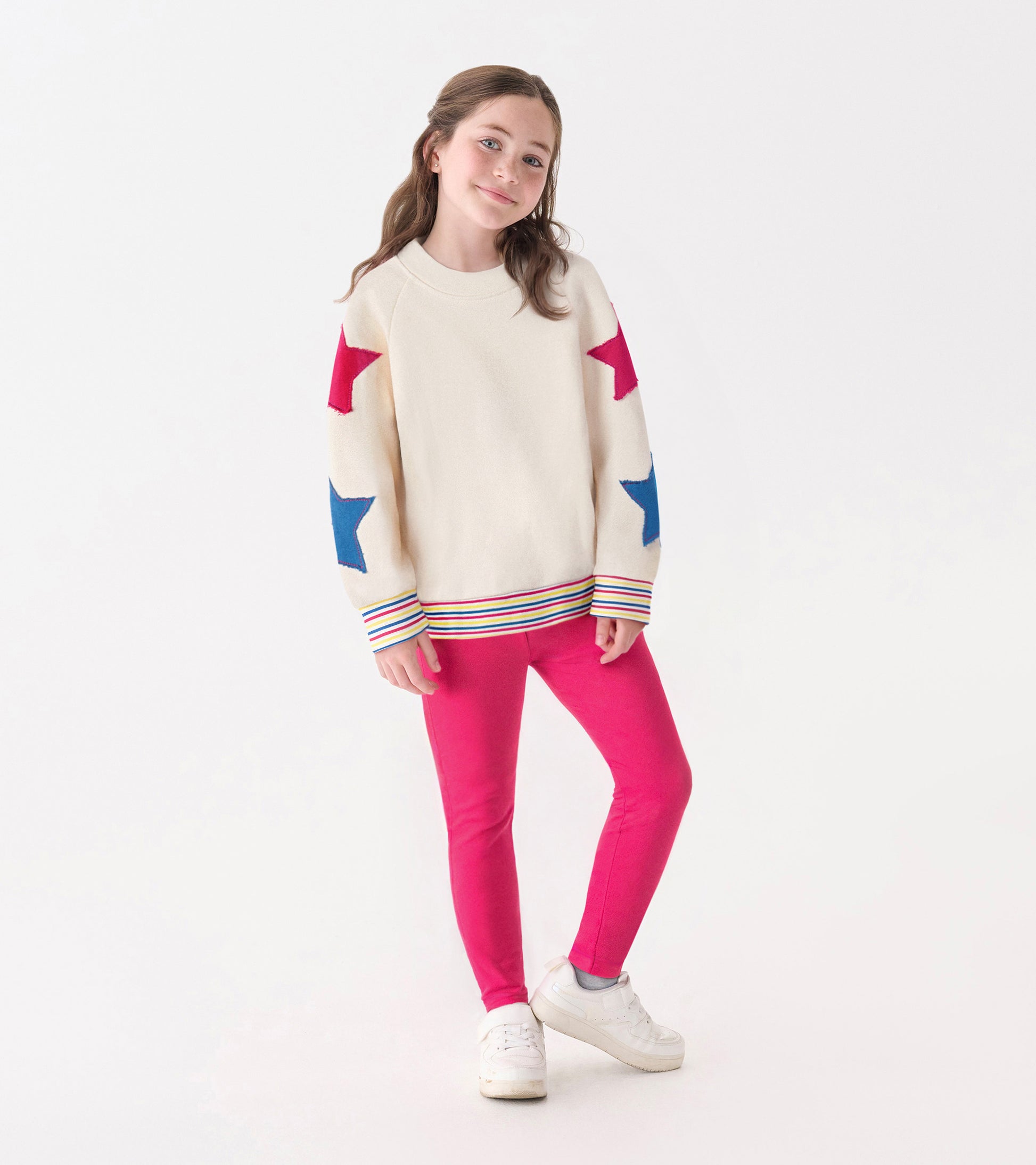 Cream pullover with colorful star patterns on sleeves, paired with pink leggings and white sneakers.