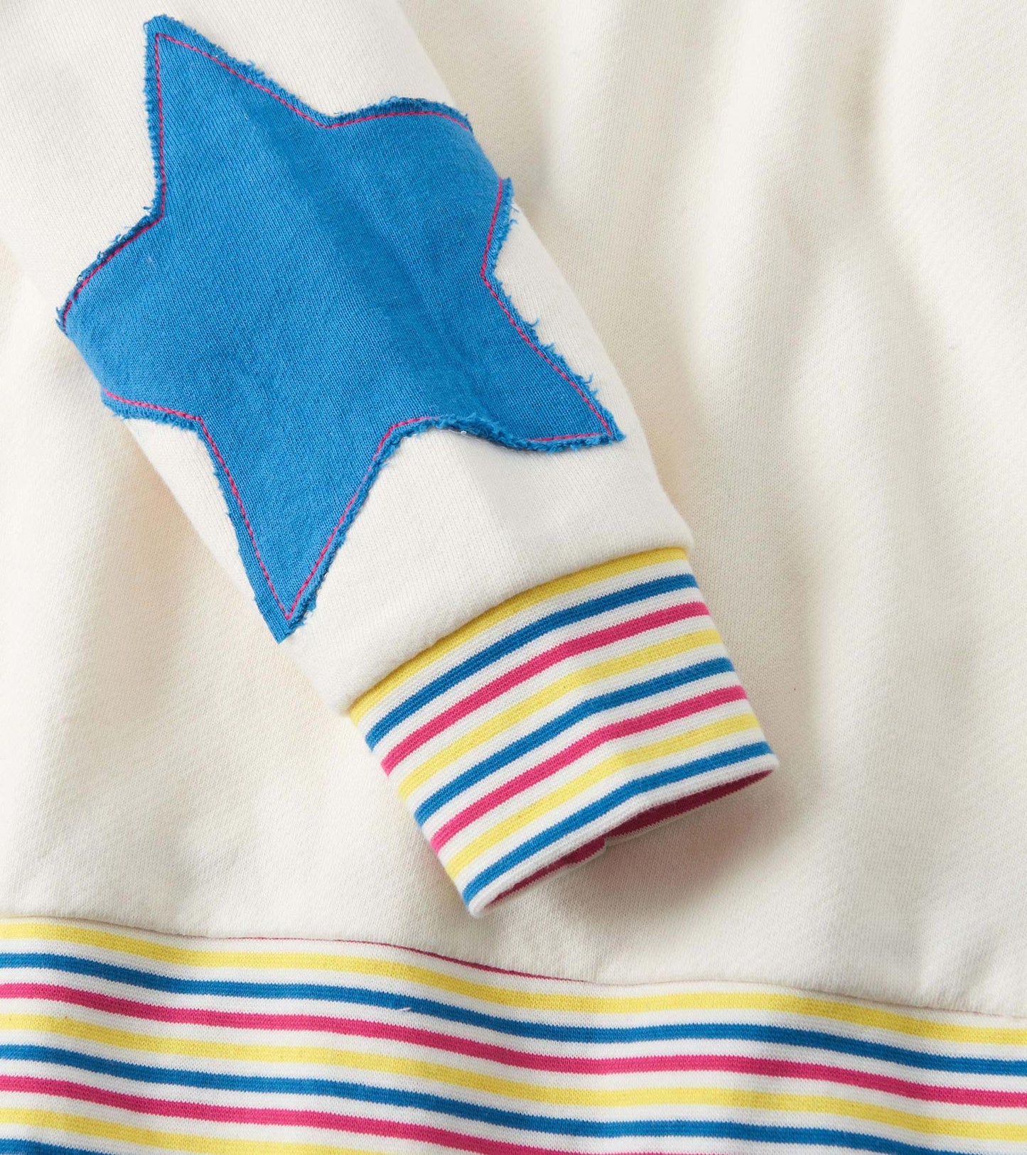 Cream pullover featuring a blue star patch on the sleeve and colorful striped cuffs and hem.