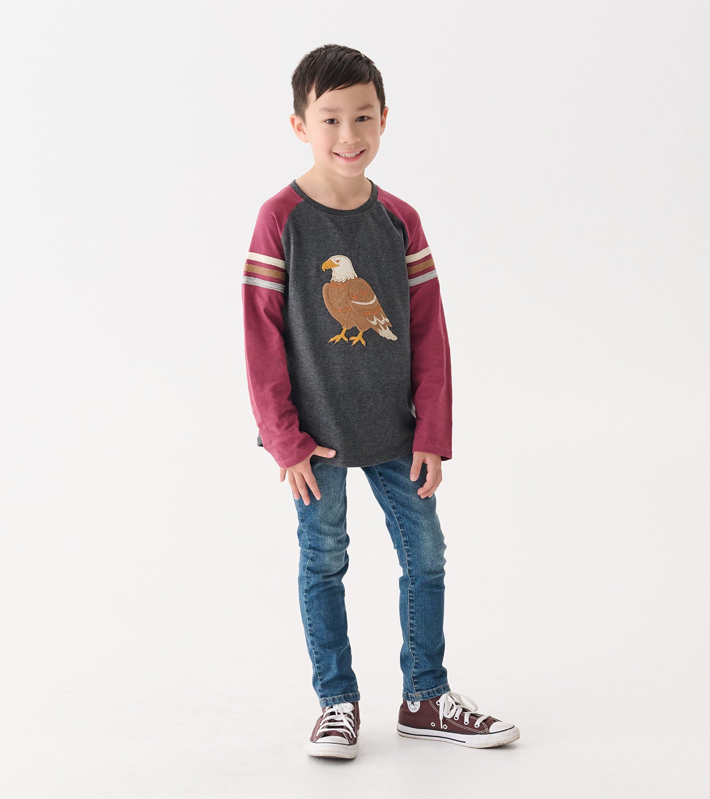 Gray long sleeve raglan t-shirt with maroon sleeves and eagle graphic, worn by a boy with blue jeans and sneakers.
