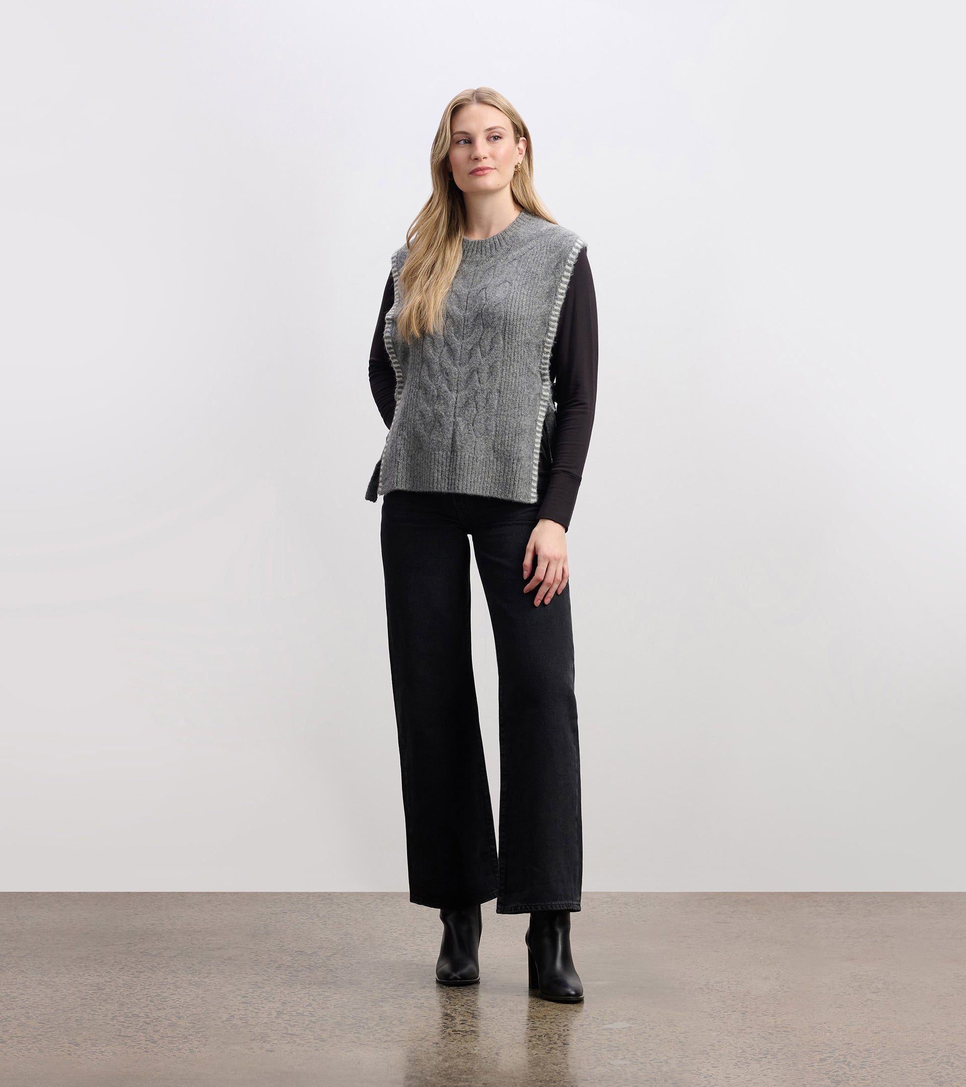 Charcoal melange side-tie sweater vest with a textured knit pattern, styled over a long-sleeve top and paired with wide-leg…