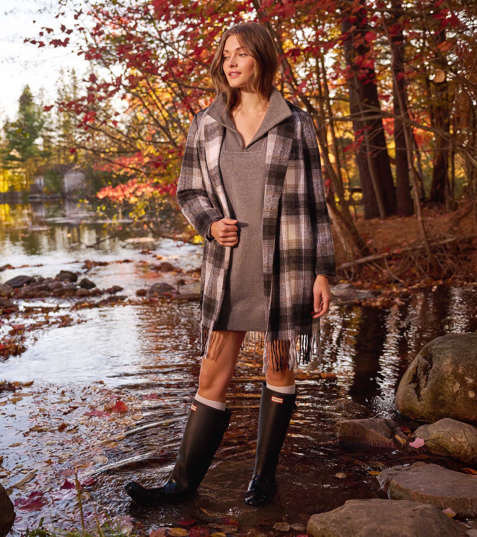Woman wearing charcoal melange notch-neck dress with plaid coat and black rain boots, standing in a stream outdoors