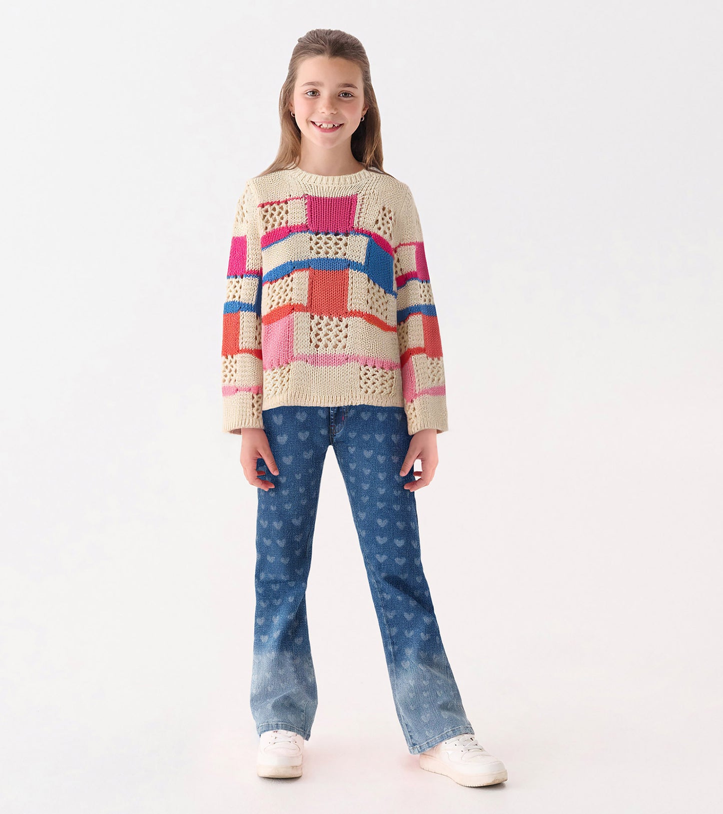Knit sweater featuring a mix of colorful patterns, paired with heart-patterned jeans and white sneakers.