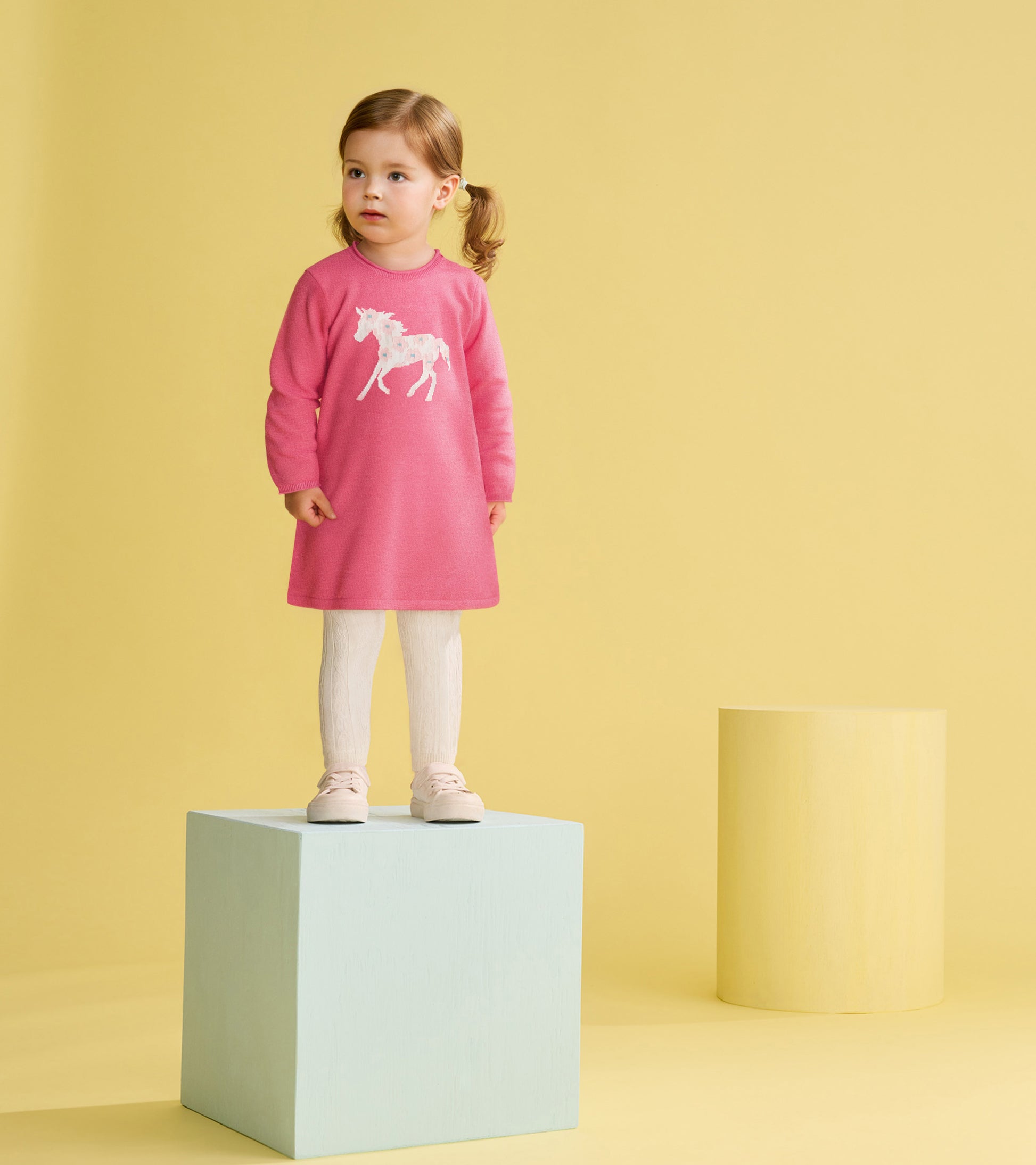 Pink sweater dress featuring a white horse design, paired with white leggings and light shoes, set against a yellow backgrou…