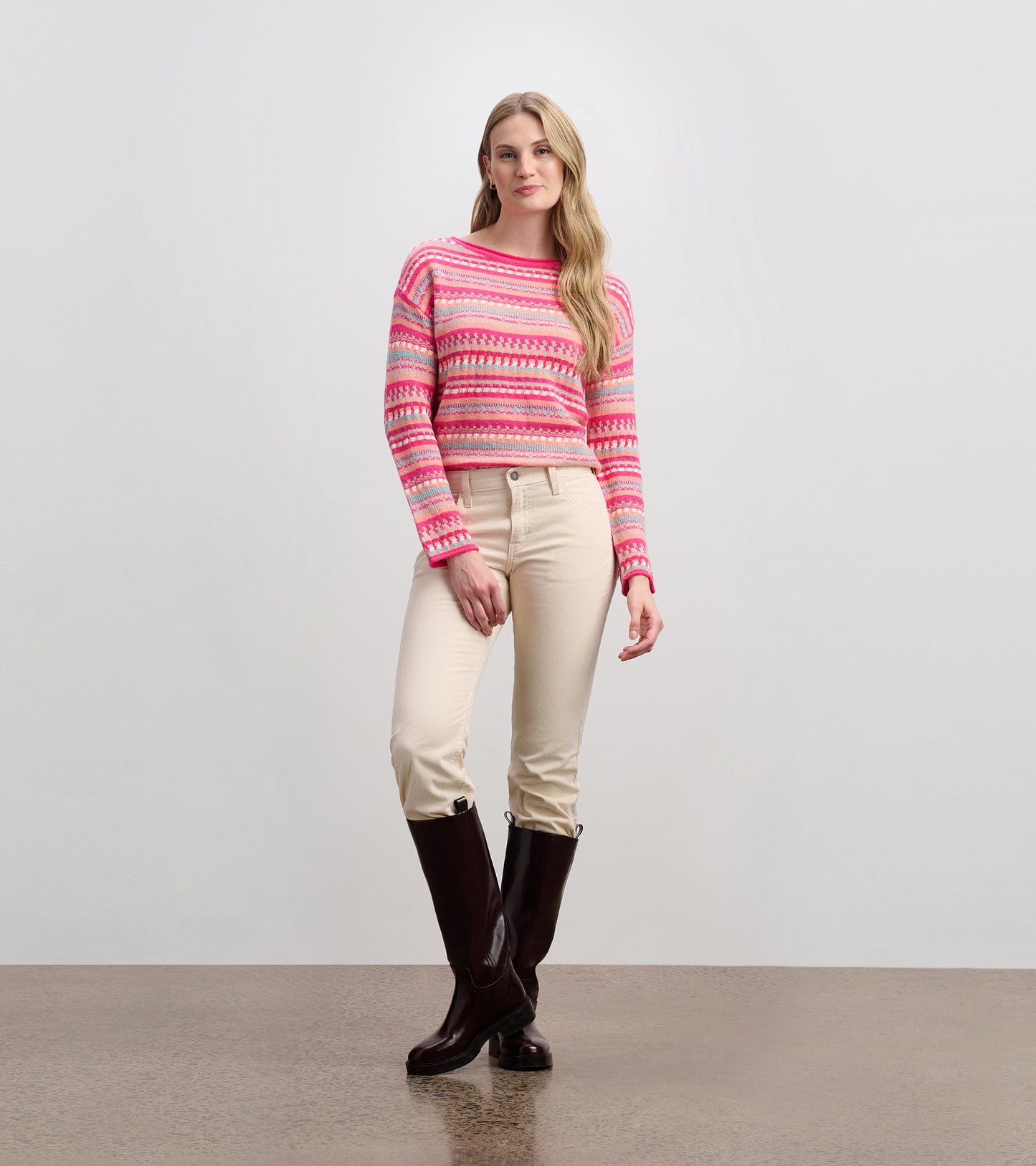 Cropped sweater in pink with multicolored patterns, paired with light-colored jeans and knee-high boots.