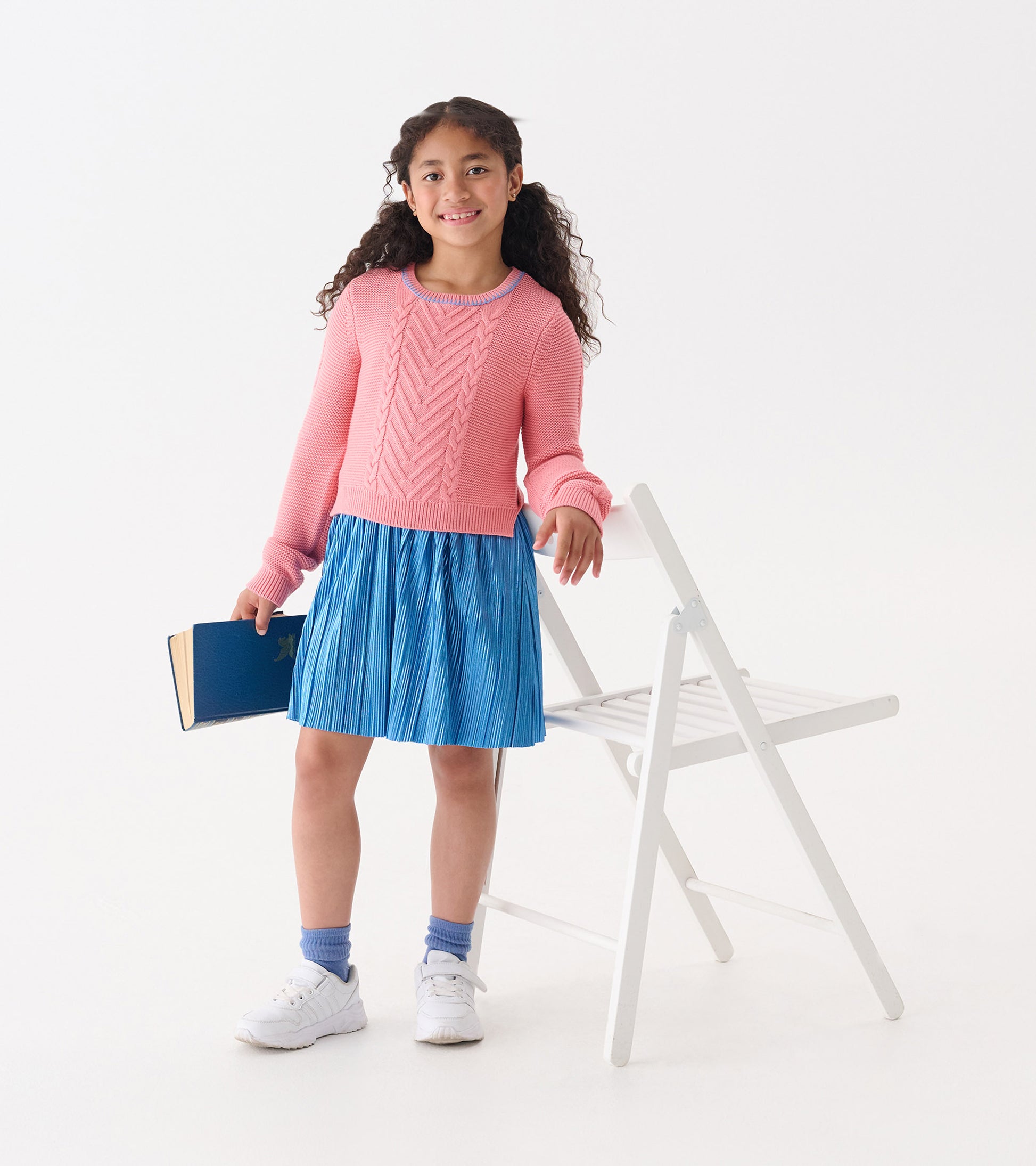 Flamingo pink knit top with textured pattern paired with a pleated blue skirt, worn by a girl holding a book.