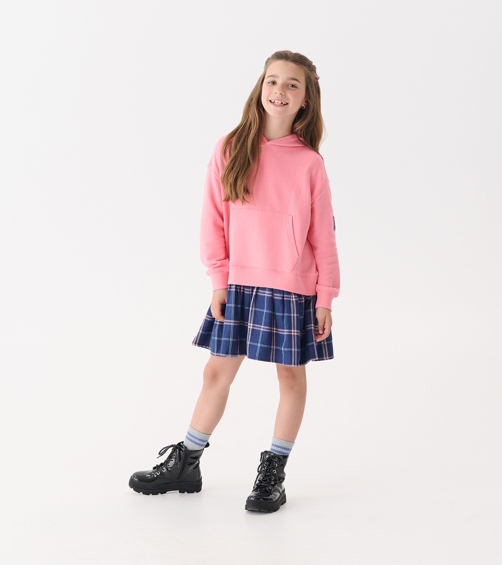 Pink hoodie paired with a navy plaid skirt, worn with black boots and striped socks, suitable for casual wear.