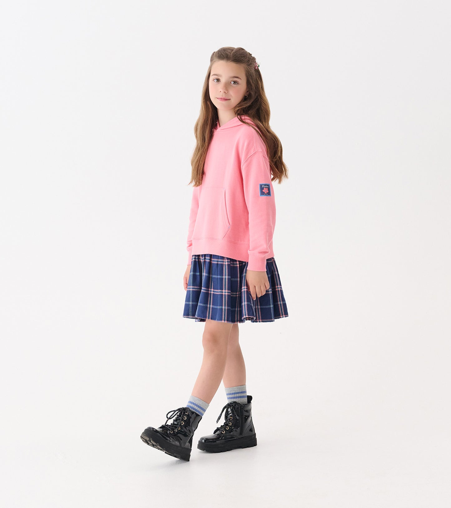 Girls' preppy plaid dress with a navy blue skirt and pink hoodie, paired with black boots and striped socks.