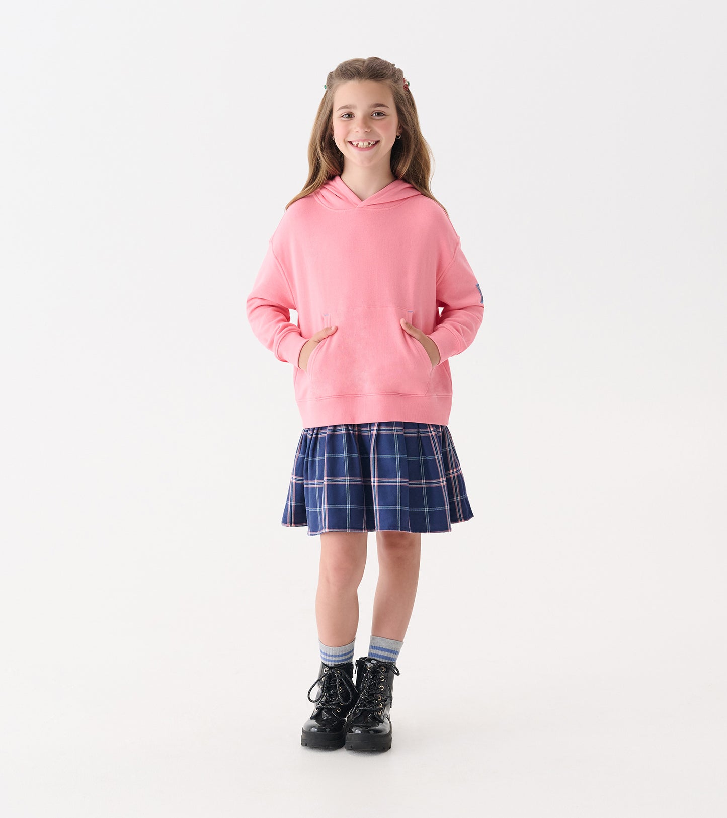 Pink hoodie with front pockets paired with a navy plaid skirt, worn with black boots and blue striped socks.