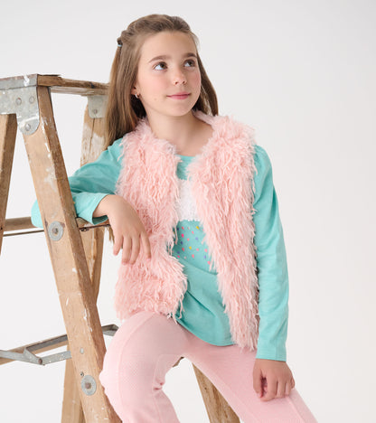 Pale pink faux fur vest worn over a teal top, paired with light pink pants, on a girl sitting beside a wooden ladder.