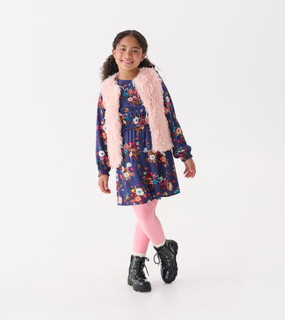 Pale pink faux fur vest worn over a floral dress, paired with pink leggings and black boots, on a smiling girl.