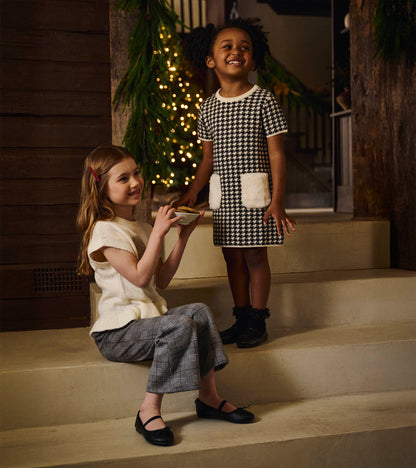 Girls black-and-white houndstooth sweater dress with white faux fur pockets, short sleeves, and crew neck