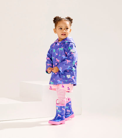 Purple rain jacket with horse and heart patterns, worn by a girl with pink rain boots and striped leggings.