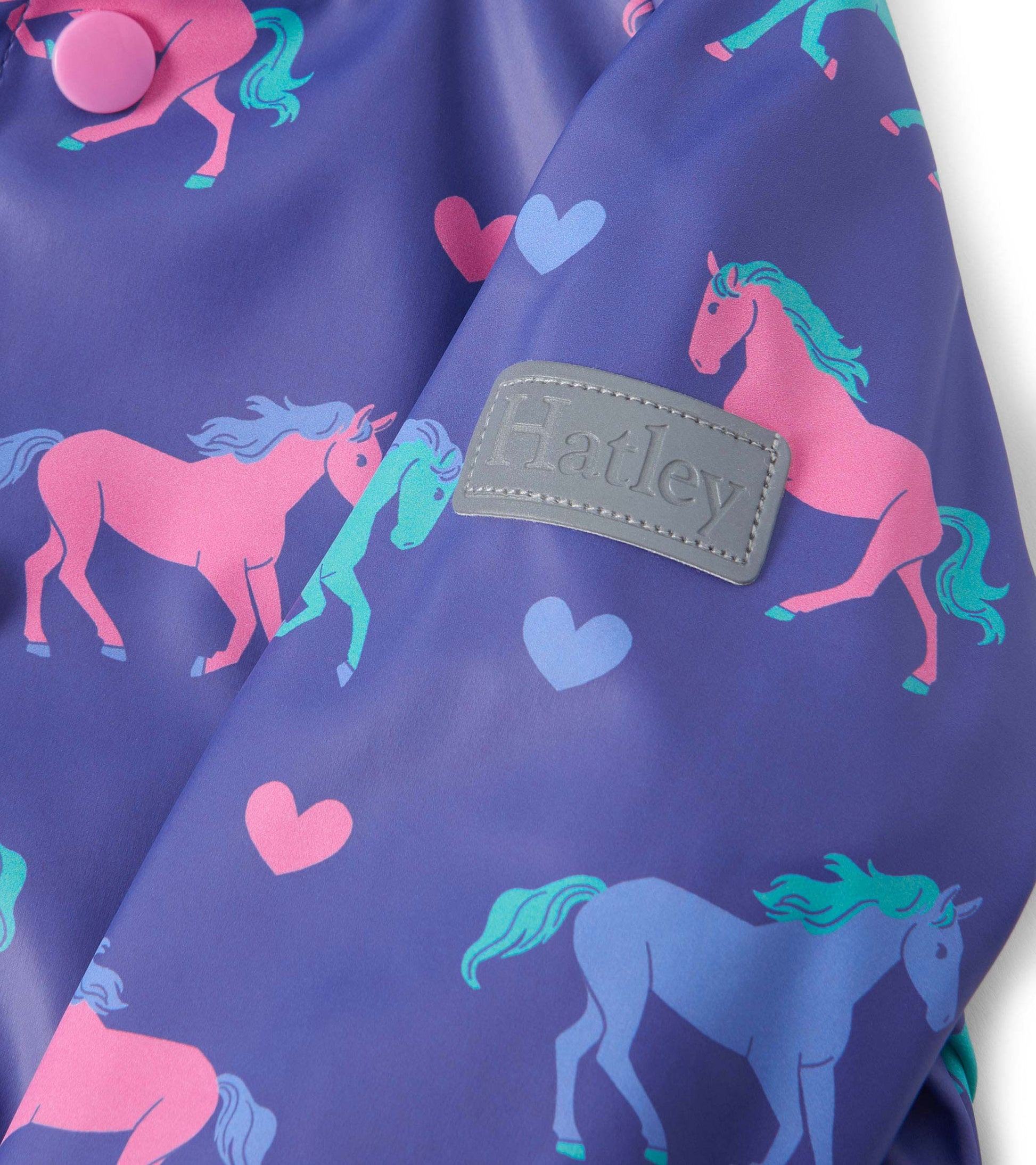Purple rain jacket featuring pink horses and hearts, with a button closure and a logo patch.