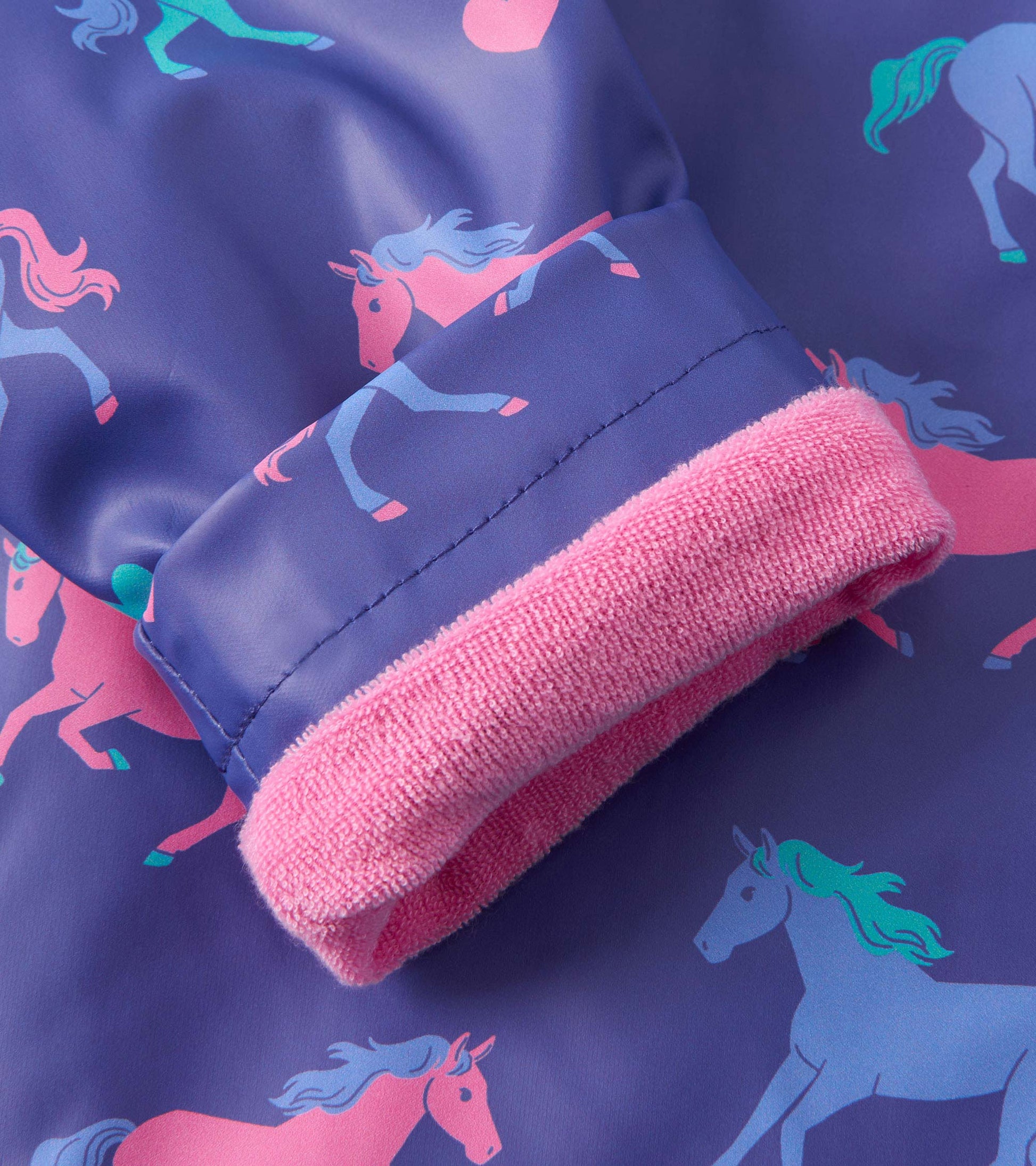 Purple rain jacket featuring playful pink and blue horse patterns, with a soft pink cuff detail.