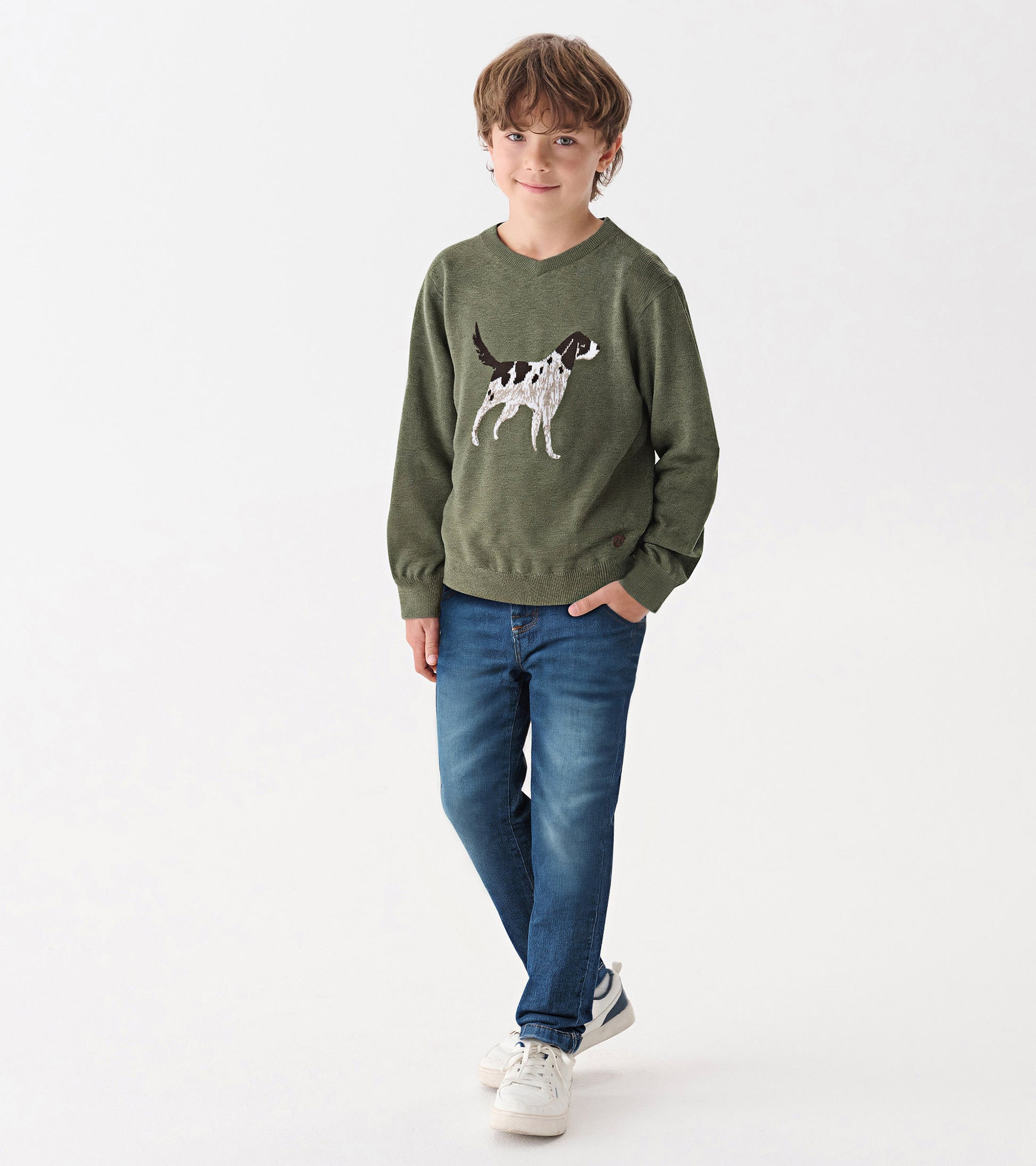 Green V-neck sweater featuring a dog graphic, worn by a boy with blue jeans and sneakers, standing against a white backgroun…