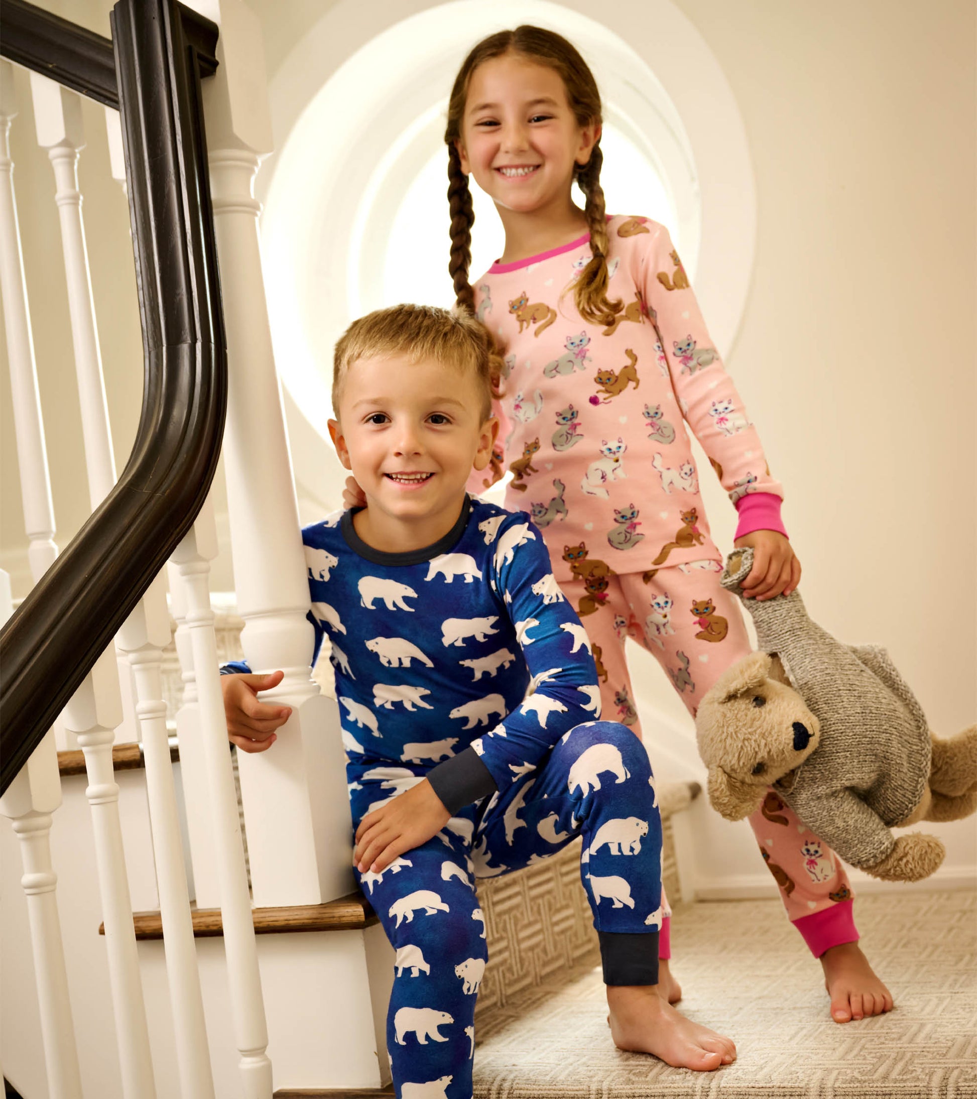 Two children in colorful cotton pajamas: one in blue with polar bears, the other in pink with playful kittens.