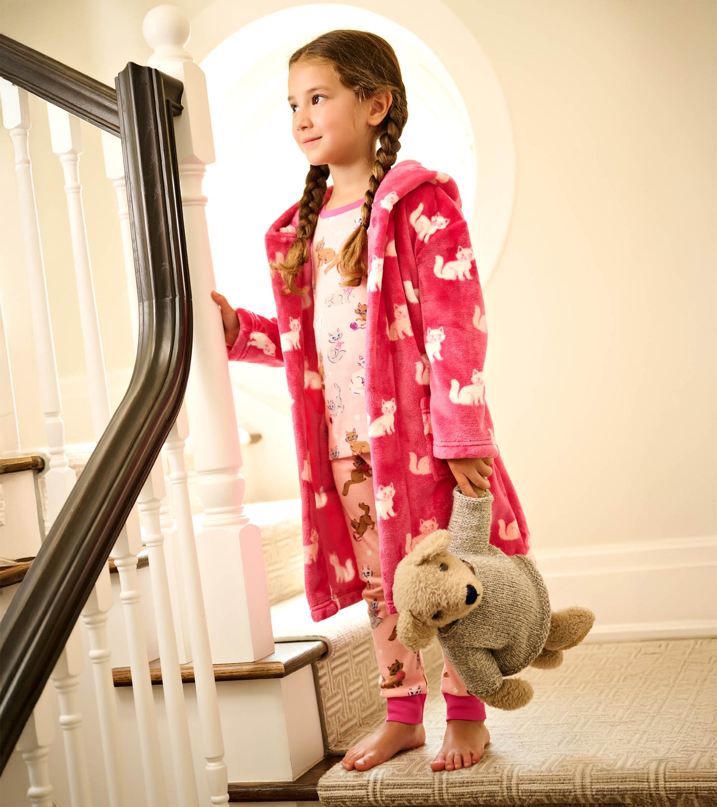 Fuzzy pink fleece robe with kitty pattern, worn by a girl holding a stuffed animal, standing on stairs.