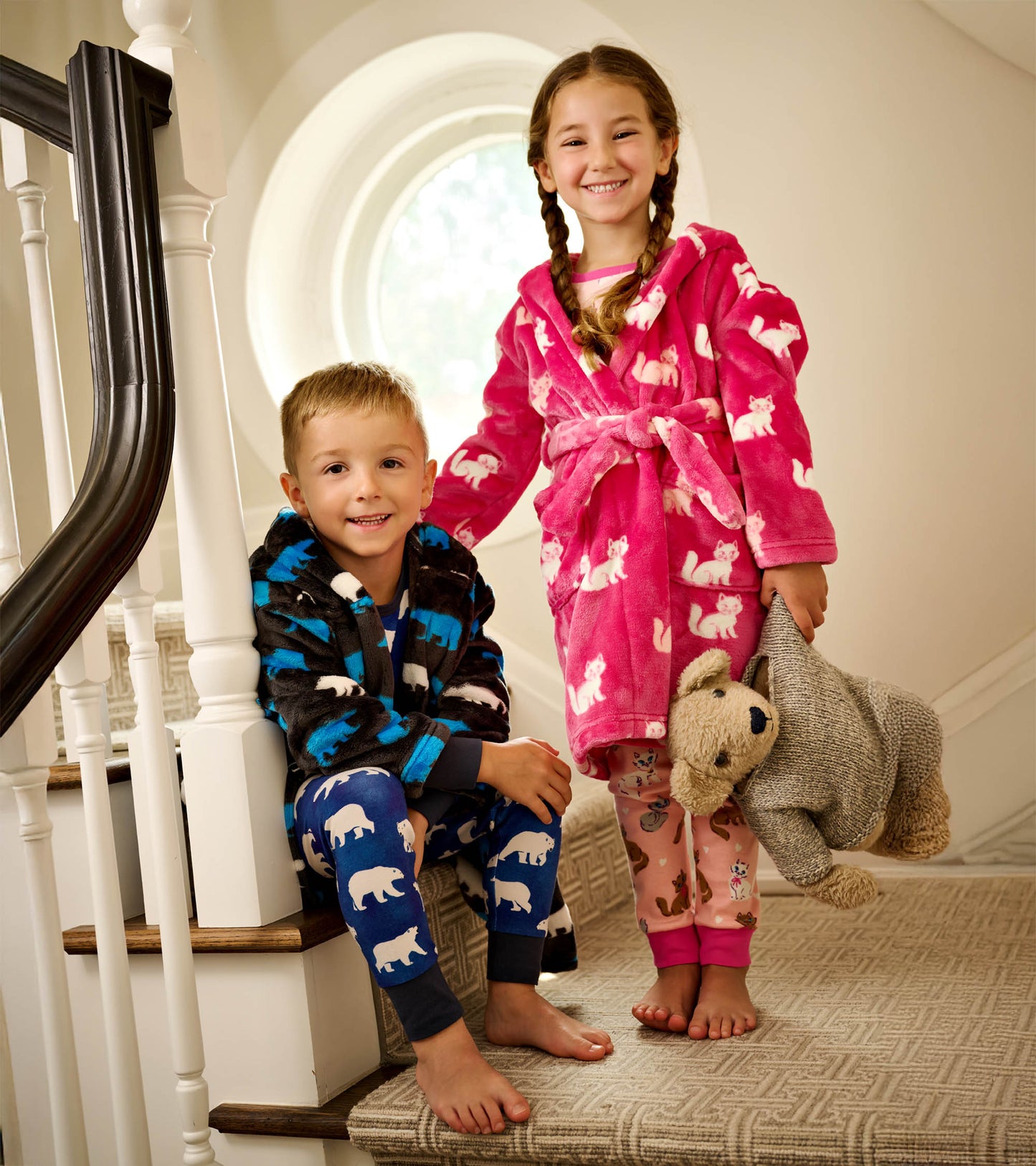 Fuzzy fleece robe in pink with white kittens, worn by a girl, paired with a boy in a black robe with blue bears.