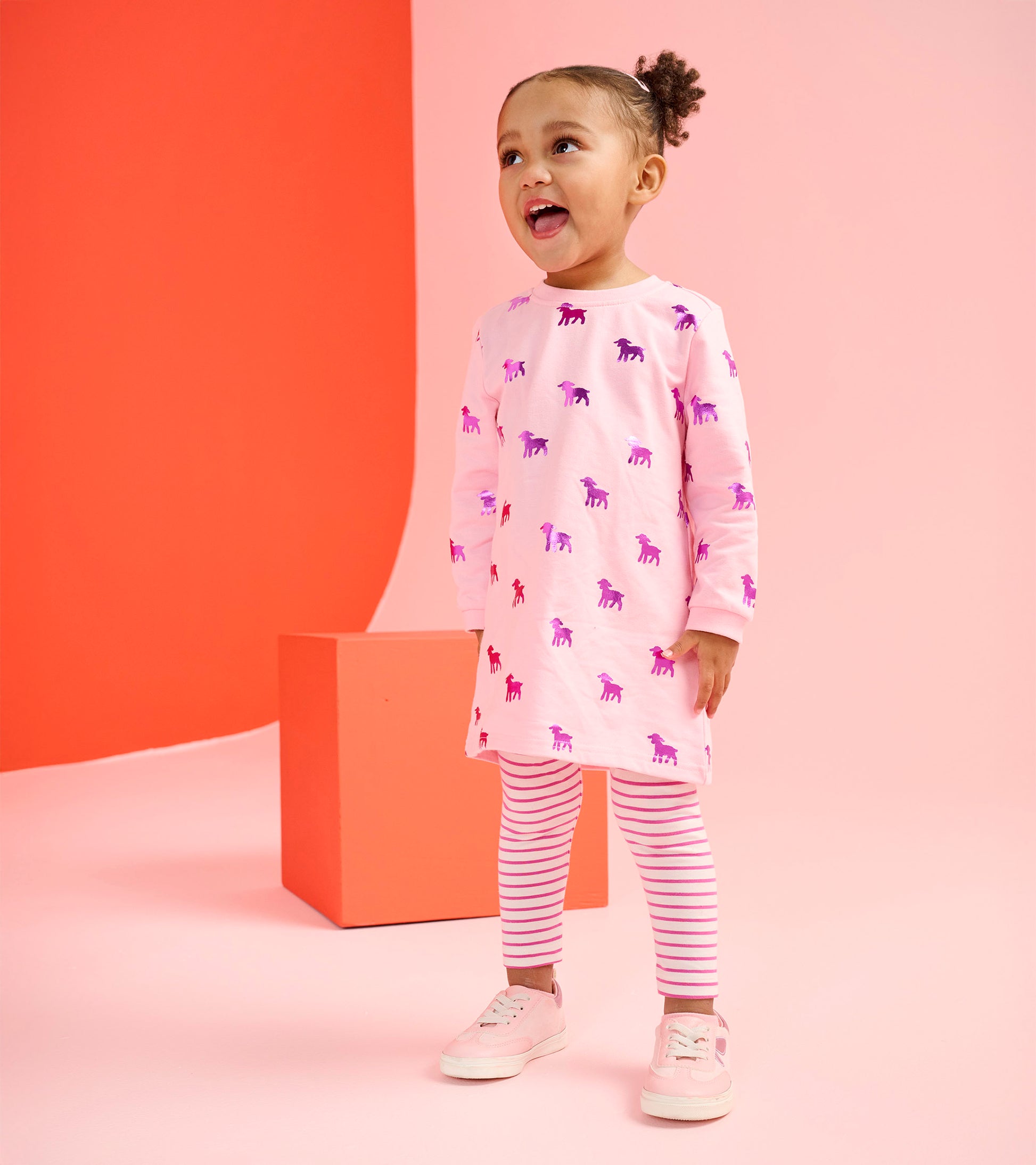 Pink dress with lamb silhouettes paired with striped leggings, worn by a smiling toddler.