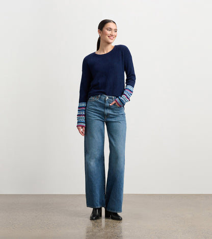 Navy sweater with colorful jacquard cuffs, paired with high-waisted jeans, worn by a model standing and smiling.