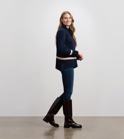 Navy mock neck sweater with pink stripes, featuring a relaxed fit and side slits, styled with jeans and knee-high boots.