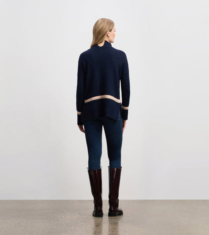 Navy mock neck sweater with a striped hem, featuring a relaxed fit and side slits, worn with dark jeans and tall boots.